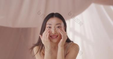 漂亮的年轻亚洲女人每天早上定期为她的脸按摩。快乐的女性微笑着，触摸着，拍拍着美丽的脸。皮肤看起来有<strong>弹性</strong>,滋润,健康.脸部按摩的概念.