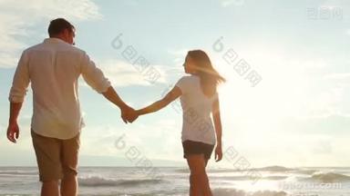 美丽的年轻夫妇手牵着手<strong>在</strong>日落时分的海滩上散步