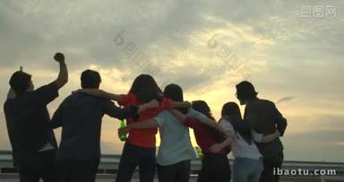 一群年轻的朋友在夏天的屋顶聚会上跳着舞, 用烤面包和闪烁的举起眼镜庆祝, 并在地面上<strong>举行</strong>日落.