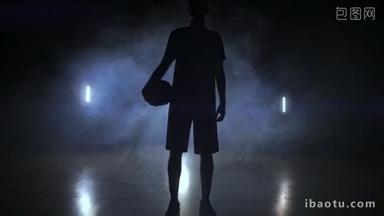 一个篮球运动员在黑暗的背景上, 在篮球场上冒出一个篮球球, 慢慢地看着<strong>镜头</strong>
