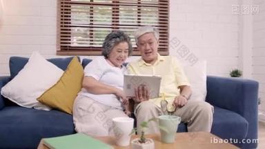 亚洲老年夫妇在家里的客厅里<strong>用</strong>平板电脑看电视, 在家里放松的时候躺在沙发上享受爱情时刻。享受时间生活方式的老年家庭在家里的概念.