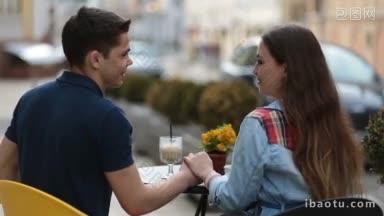 背影的快乐爱的夫妇手牵着手，交谈，坐在街头露天咖啡馆年轻夫妇的爱