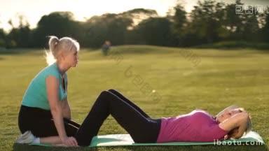 侧面美丽的健身高级妇女做腹部仰卧起坐，在公园草坪垫子上压锻炼，而女朋友
