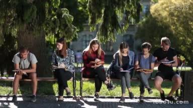 一群忙碌的大学生坐在校园公园的长椅上看书，看讲稿