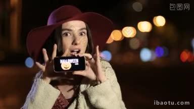美丽的深色头发女人在波多帽子显示手机与特别提供万圣节销售在<strong>夜晚</strong>城市<strong>街道</strong>的屏幕上