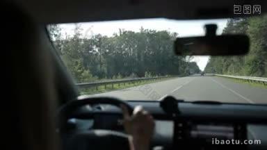从汽车内部的阳光视角看，一<strong>名</strong>女子在高速公路上驾车穿过森林