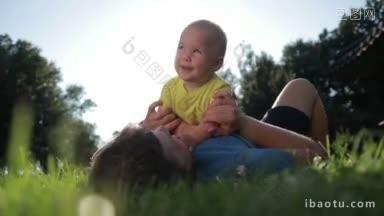甜美的婴儿男孩蓝色的眼睛坐在父亲的胸部和微笑的光芒惊人的夕阳，而