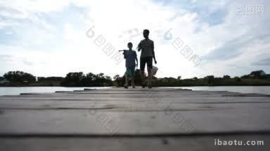 无忧无虑的父亲和十几岁的儿子穿着短裤，肩上扛着钓鱼竿，沿着木制浮筒走着去钓鱼