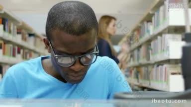 一名非洲裔美国大学生在图书馆<strong>看书</strong>，<strong>背景</strong>是一名白人妇女从书架上取书