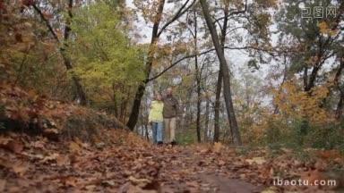 英俊的老人拥抱着他心爱的美丽的妻子在秋天公园散步，老夫妇在散步