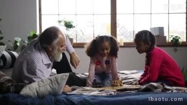 英俊的大胡子爷爷和可爱的混血儿孙女在家里的床上下棋，积极的爷爷教孙子们下棋