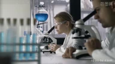 <strong>迷人</strong>的研究科学家在显微镜下观察生物样本，她的男同事在背景研究人员进行科学研究