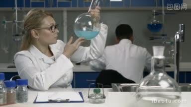 女研究员在化学实验室进行研究，迷人的女科学家戴着保护眼镜，拿着一个装有蓝色液体的<strong>烧瓶</strong>