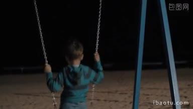 男孩独自在海滩游乐场荡秋千，夜晚的场景与黑暗的大海在一个孩子的面前