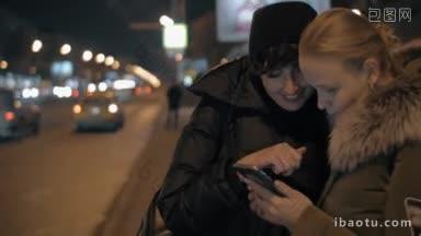 两名妇女在公共交通车站等车，用智能手机上网