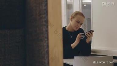 年轻女子在咖啡馆里用手机，她坐在桌子旁打字短信或在网上聊天