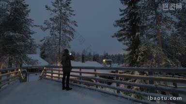 男子游客在冬季度假胜地的夜晚用<strong>手机</strong>拍摄雪景和高高的松树