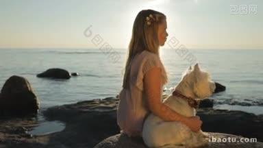 一个悲伤的小<strong>女孩</strong>带着一只狗坐在海边的石头上看日落