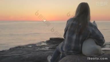 一个悲伤的小女孩带着一只狗坐在海边的石头上看日落