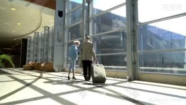 年长的游客夫妇提着旅行箱在机场边走边聊天