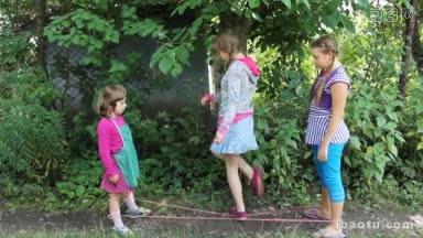 两个快乐的女孩站着，中间拉着橡皮筋，第三个妹妹跳过橡皮筋