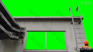 工人爬上金属梯子到房子，从屋顶的绿色屏幕出去