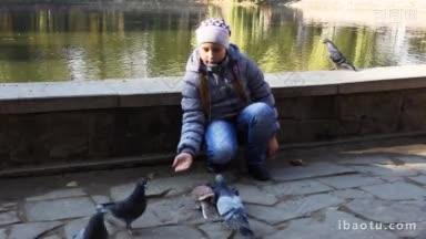 可爱的少女在湖边的秋季城市公园里喂爆米花鸽子