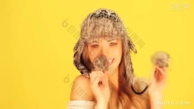 活泼的笑着的金发女人玩着一顶<strong>毛绒</strong>绒的冬天帽子上的<strong>毛绒</strong>球