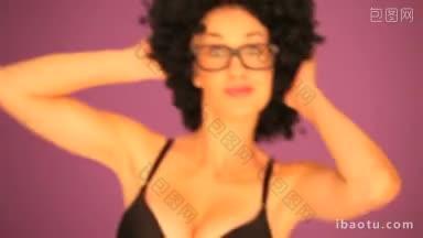 在紫色的背景下，一个女人戴着大大的黑色卷曲的非洲式发型和眼镜进入了焦点