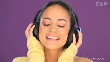 美丽活泼的褐发女子戴着耳机，在紫色的录音棚背景下听音乐