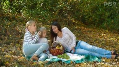 年轻的母亲和两个女儿在秋天的公园野餐，边说边吃水果
