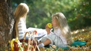 两个金发小女孩在<strong>树下</strong>享受阳光明媚的日子，<strong>看书</strong>和吃苹果