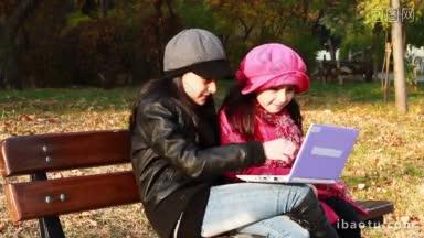 两个女孩坐在长凳上玩笔记本电脑姐妹在笔记本电脑上玩得很开心