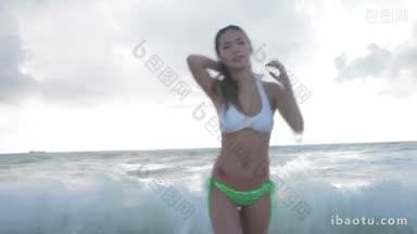 穿着比基尼的年轻美女从海里走到镜头前身后有个波浪
