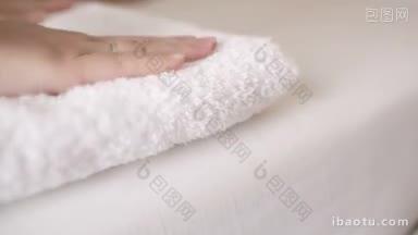 女人把干净干净的白毛巾放在床上，然后用手抚平它