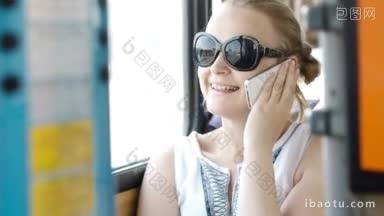 快乐迷人的年轻女子戴着太阳镜在她的智能<strong>手机</strong>上说话，在乘公共汽车旅行时高兴地微笑