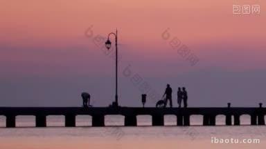 一家人在海边的码头上遛狗，夕阳映衬着<strong>朦胧</strong>的粉红色天空，海面平静