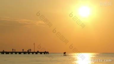 日落时分，人们在平静的海面上冲浪或帆板，与壮观的鲜艳的橙色天空相映衬