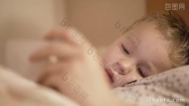 近距离的肖像三岁的男孩躺在床上与他的母亲和看卡通片智能