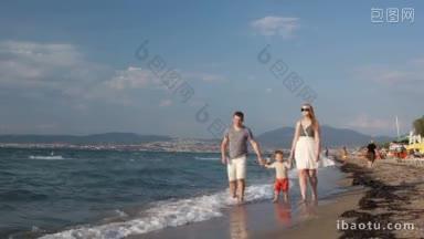 年轻的一家人在海滩上散步，一个可爱的小男孩牵着他的<strong>妈妈</strong>和爸爸的手