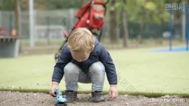 小男孩在<strong>户外</strong>玩玩具挖掘机，然后在红色婴儿车的背景下离开操场