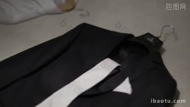 黑色结婚礼服放在架子上，<strong>白色领带</strong>和手帕在床上准备好