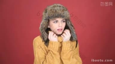 美丽的年轻女子戴着一顶温暖的毛皮帽子，忍受着寒冷，皱着眉头，<strong>因为</strong>她偎依在polo衫里