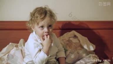 小可爱的卷毛男孩坐在床上看电视，把手指放进嘴里