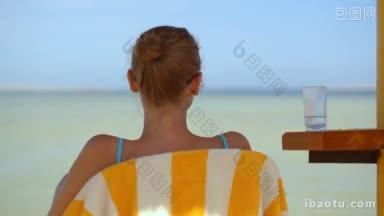 一个女人坐在沙滩上的椅子上喝水的背影