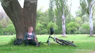 骑自行车的女孩<strong>坐在树下</strong>在公园听音乐