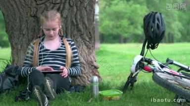 十几岁的女孩骑自行车<strong>坐在树下</strong>使用平板电脑