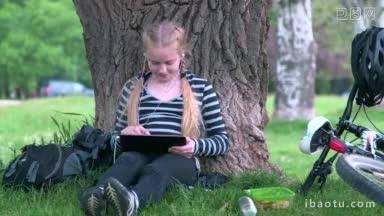 十几岁的女孩骑自行车坐在树下使用平板电脑