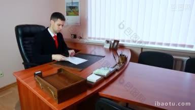穿着西装打着红领带的年轻英俊的经理阅读文件并签字
