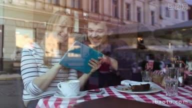 幸福的年轻夫妇使用<strong>触摸</strong>板在咖啡馆通过玻璃与城市的倒影